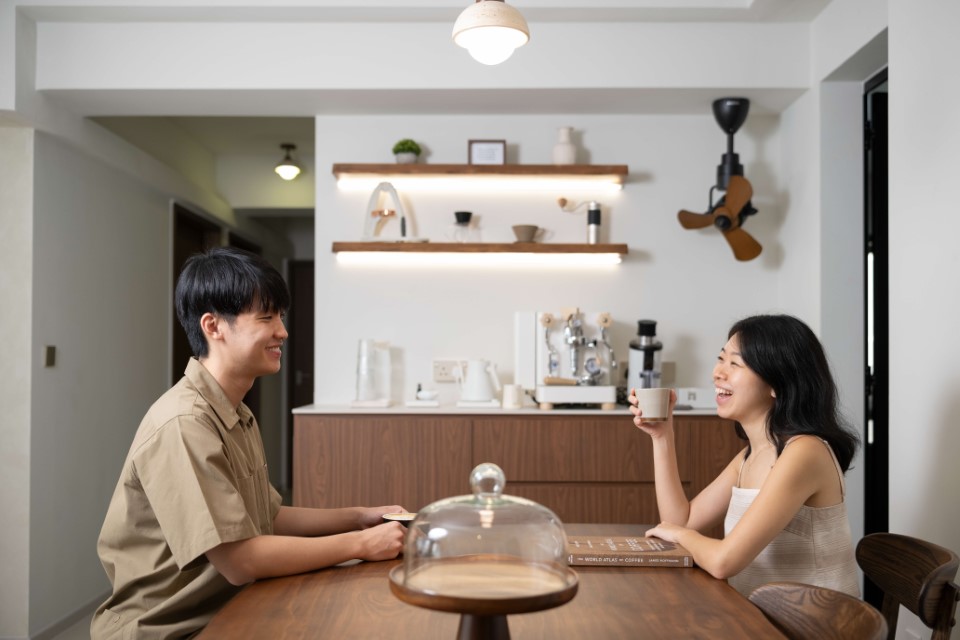 A happy couple seated facing each other at the dining table of their newly renovated HDB flat